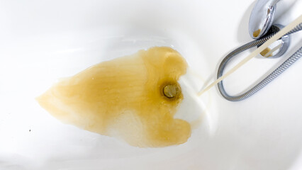 Brown dirty water flowing from shower into bathtub, concept of water pollution and plumbing problems at home