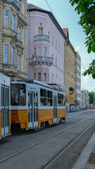 Classic yellow and white tram in Budapest passing through historic buildings along a quiet city street.