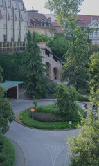 Stone medieval-style structure with arched entrances nestled in lush greenery near a modern building in Budapest.