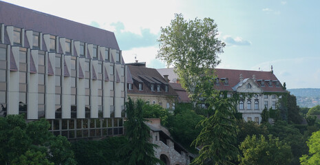 Contrasting architectural styles in Budapest: a modern glass building alongside historic baroque and neoclassical structures, surrounded by lush greenery.