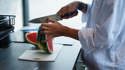 Chef slicing watermelon on a cutting board, preparing a refreshing summer dish in a modern kitchen