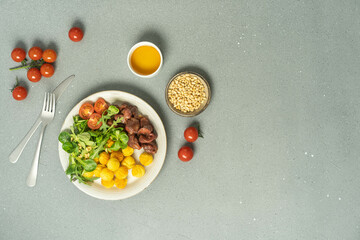 Plate with salad, chicken, juice and seeds on light grey.