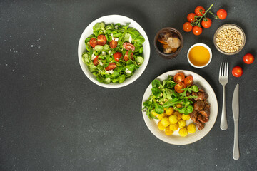 Two plates with salad and chicken on dark black background.
