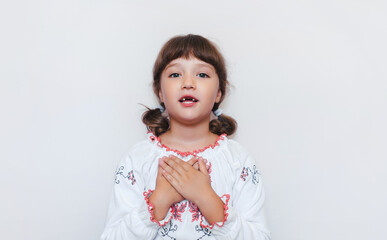 A little Ukrainian girl in white embroidered embroidery against the background of the wall performs...