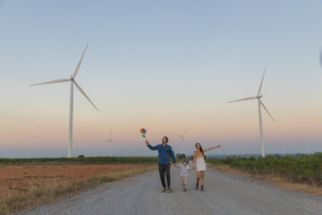 Family with son walking on field on wind farm. Happy Family and son playing at the Wind turbines generating electricity. Family time together.