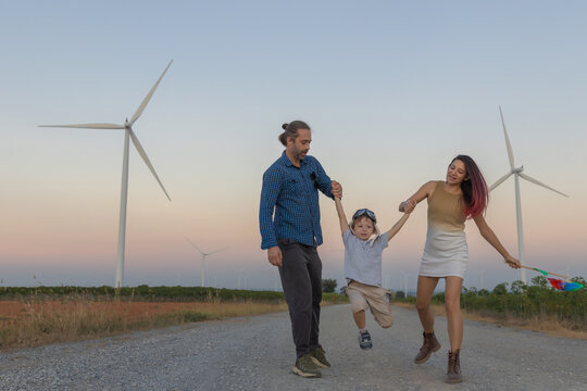 Family with son walking on field on wind farm. Happy Family and son playing at the Wind turbines generating electricity. Family time together.