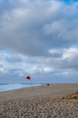 Red warning flag on sandy beach in Nazare, Portugal. Lifeguard patrol vehicle visible in background...