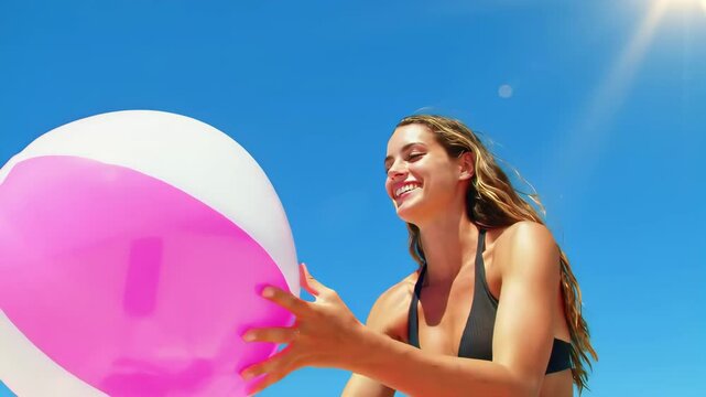 Smiling Young Woman in Black Bikini Playing with Pink White and Blue Beach Ball on Bright Sunny Day with Blue Sky Background