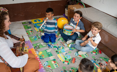 Preschool children play drums and shakers with their teacher during a lively classroom activity. A...