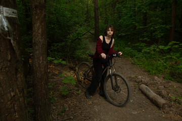 Naklejka premium Beauty woman biking on bicycle on spring trees green forest background, looks happy. Fun sport girl outdoors. Female cyclist riding in park. Full lenght portrait. Natural real colors, contrast, light
