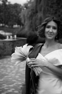 Black and white portrait of a smiling bride wearing a leather jacket and holding flowers, captured in a candid outdoor moment.  Smiling Bride in Leather Jacket &mdash; Black and White Portrait
