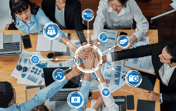 A diverse business team collaborates around a wooden table equipped with technology, engaging with charts and digital tools to drive innovative solutions and success. Amity - Powered by Adobe