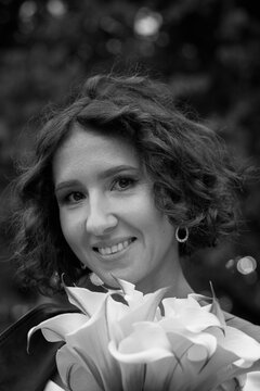 Black and white portrait of a smiling bride wearing a leather jacket and holding flowers, captured in a candid outdoor moment.  Smiling Bride in Leather Jacket &mdash; Black and White Portrait
