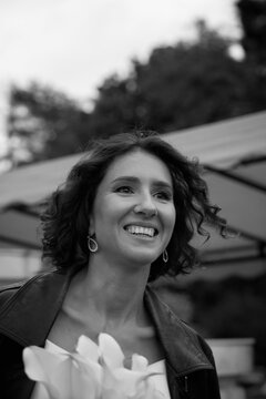 Black and white portrait of a smiling bride wearing a leather jacket and holding flowers, captured in a candid outdoor moment.  Smiling Bride in Leather Jacket &mdash; Black and White Portrait