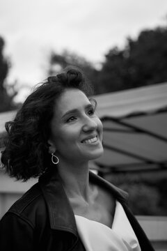 Black and white portrait of a smiling bride wearing a leather jacket and holding flowers, captured in a candid outdoor moment.  Smiling Bride in Leather Jacket &mdash; Black and White Portrait