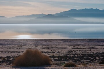 Sunrise over the Salton Sea in California, USA. The sun reflects off the calm water, with mountains...