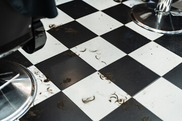 Hair clippings scattered on a black and white tiled floor in a salon