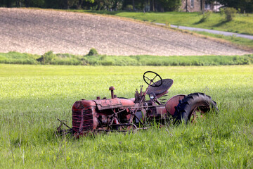 Side view of deserted rusty antique farming tractor discarded in a field in southern Ontario Canada