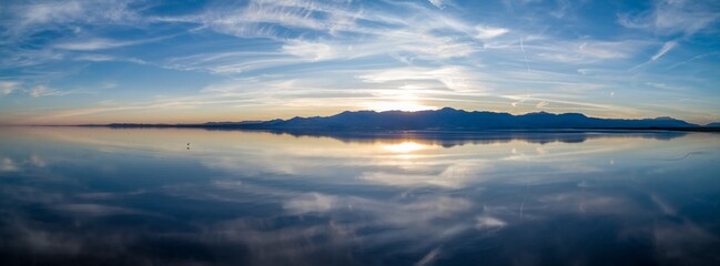 Fototapeta premium Sunset overSalton Sea, Mecca, California, USA. The sun reflects off the calm water, creating a mirror image of the sky and mountains. The scene evokes peace and tranquility.