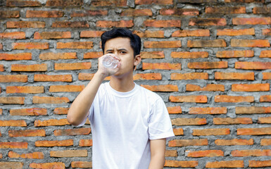 portrait of asian man drinking bottled water with brick wall background