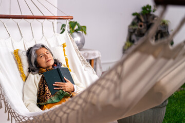 Senior woman resting in hammock with book, enjoying peaceful retirement