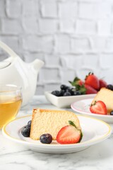 Pieces of tasty bundt cake with berries and tea on white marble table, closeup