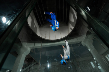 A male instructor teaches a woman how to fly in a wind tunnel. Free fall simulator.