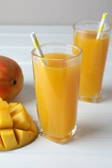 Tasty mango juice in glasses and fresh fruits on white wooden table, closeup