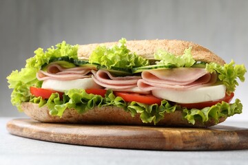 Tasty baguette sandwich with ham and vegetables on light grey table, closeup