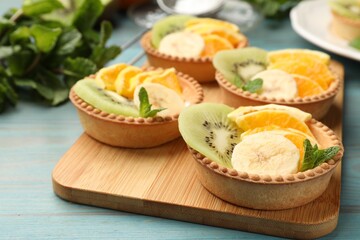 Tartlets with fruits and mint on light blue wooden table, closeup. Delicious dessert