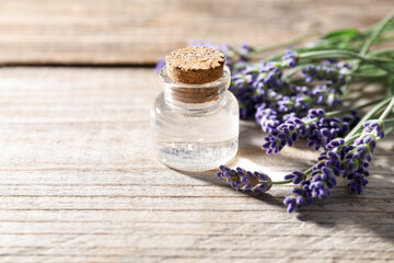 Natural essential oil and lavender flowers on wooden table, closeup. Space for text