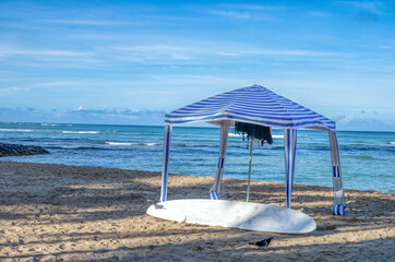 Blue and White Beach Cabana with a White Surfboard on an Empty Ocean and Beach.
