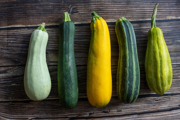 whole fresh different yellow, white, striped and green zucchini's in row on wooden background. Top view flat lay, close up
