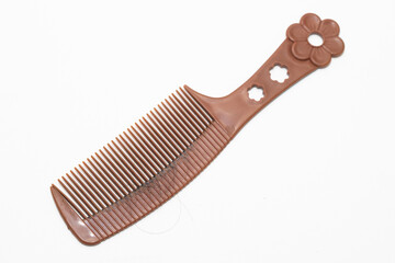 A brown plastic comb with a flower handle design lies on a white background, featuring fine teeth and a few strands of hair.