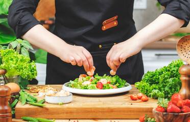 Chef prepares a colorful salad with greens and shrimp, actively arranging ingredients in a warm kitchen filled with fresh produce.