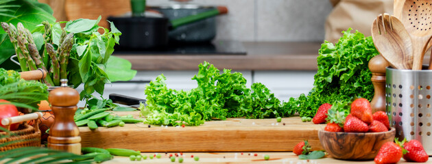 Healthy vegan cooking in a bright kitchen with green lettuce, fresh vegetables and herbs prepared...