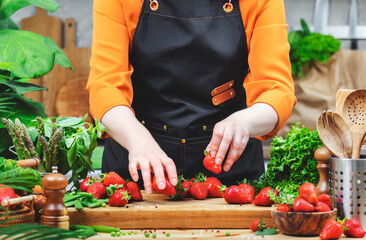 Chef prepares fresh strawberries in vibrant kitchen filled with green vegetables and cooking...