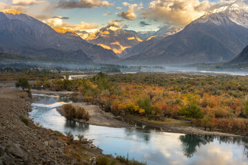 A serene river winds through a mountain valley, lined with golden autumn trees and bathed in the soft, warm light of evening.
