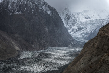 A massive glacier snakes through rugged, towering mountains. The icy expanse contrasts with the...