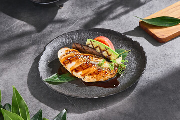 Grilled chicken fillet on a dark plate, bright natural lighting, minimal overhead composition