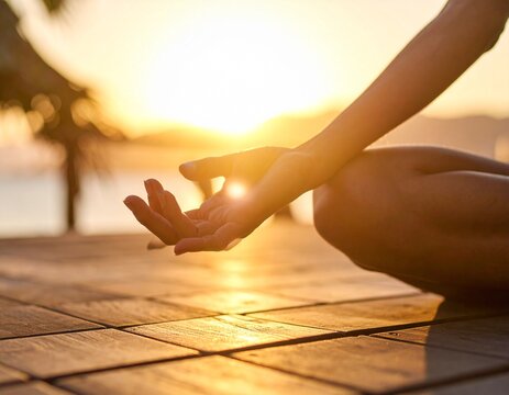 Close-up of hands in a meditative pose during yoga on a wooden deck at golden hour.