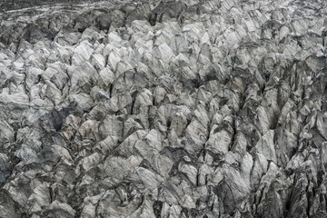 An abstract view of a glacier’s surface showcasing tightly packed ice pinnacles, deep cracks, and natural patterns in shades of gray and white.