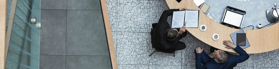Header of business meeting with participants reviewing documents and using devices at a round table. Focus on collaboration and professional environment
