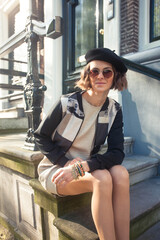 Fashionable young woman in beret cap sitting on the stairs in front of typical Dutch building in Amsterdam