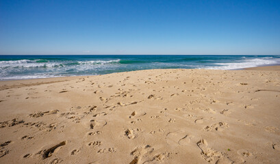 A popular tourist beach scene. Lots of footprints in the sand where people and dogs have been. With copy space.