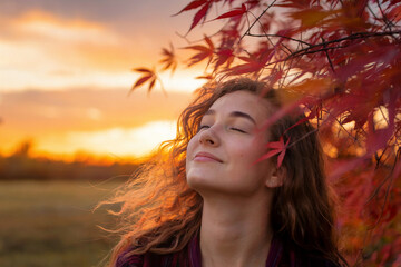A serene autumn portrait at sunset featuring a young woman with long wavy brown hair backlit by warm golden light. 