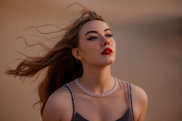 A close-up portrait photograph of a young woman with flowing brown hair caught in motion against a warm beige background. 