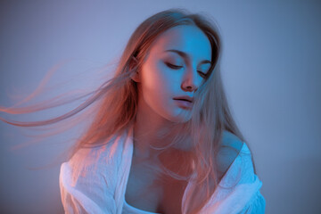 A moody portrait photograph with blue and pink lighting. A young woman with long blonde hair flowing to the left side of the frame, captured with motion blur.
