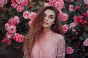 A portrait photograph of a young woman with long, flowing brown hair against a backdrop of pink roses.