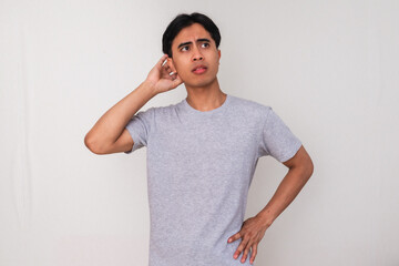 Confused young Asian man standing and scratching his head while looking up with a puzzled expression, isolated on white background. Perfect for concept and advertisement use